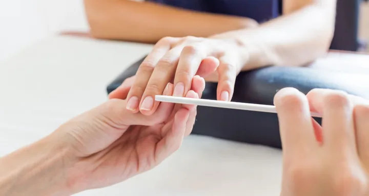 A close-up of hands during a manicure session, with one hand using a nail file on the other's nails.