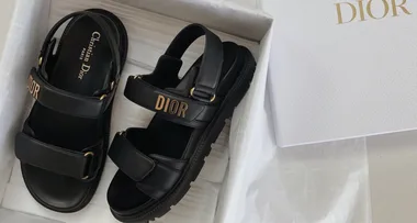 Black Dior sandals with gold-tone "DIOR" logo, black insoles with "Christian Dior Paris" text, in a white Dior box.