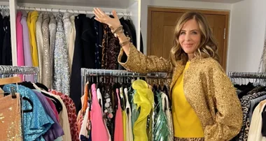 A woman wearing a gold sequin jacket gestures towards a colorful wardrobe filled with various clothes.