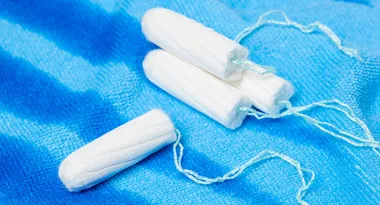 Four white tampons with strings on a blue textured surface.