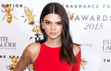 A person in a red dress at the Fragrance Foundation Awards 2015 with a backdrop featuring bees.