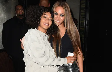 Two women smiling and embracing each other at a nighttime event, one holding a phone, with a blurred background.