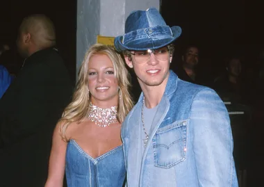 Two people in coordinated denim outfits, one with a dress and the other with a jacket and hat, at an event.