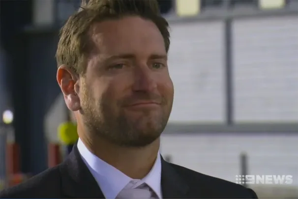 A man in a suit with a faint smile, standing outdoors. The image is credited to 9 News.