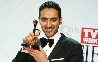 Person in a suit smiling and holding a gold TV Week Logie award.