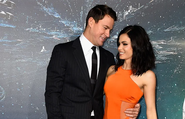 A man in a suit and a woman in an orange dress smiling at each other on a sci-fi themed backdrop.