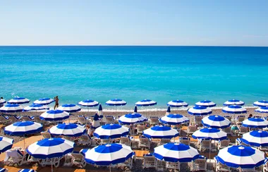 Beach scene with rows of blue-and-white umbrellas and a clear blue sea in the background.