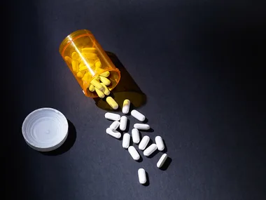 Prescription bottle tipped over, spilling white pills on a dark surface.
