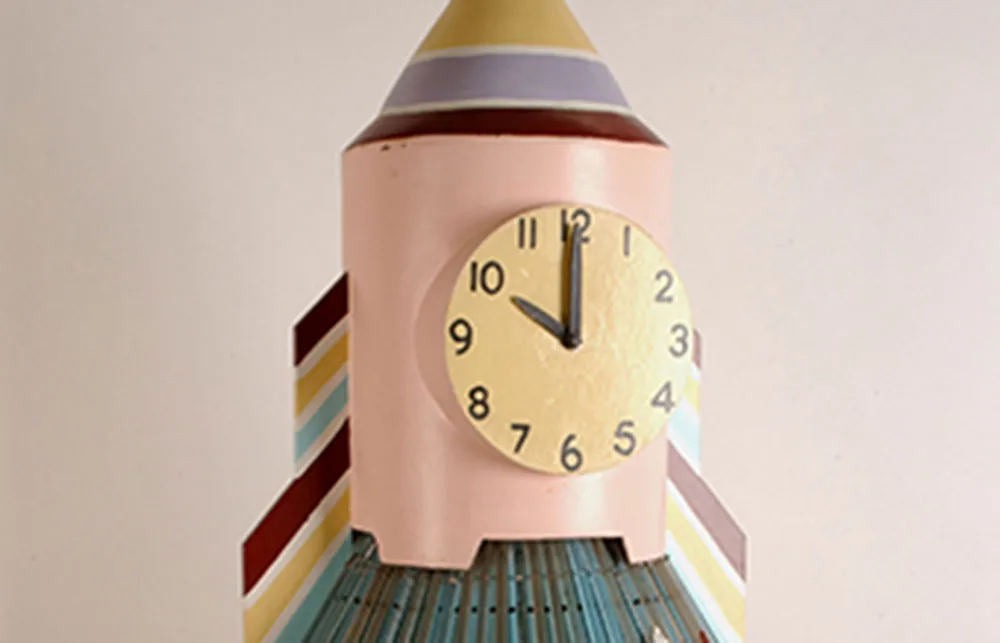 Colorful rocket-shaped clock with a yellow face, showing 10:10. Striped design, pastel pink, and yellow accents.