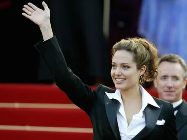 Woman in a formal suit waves happily on a red carpet.