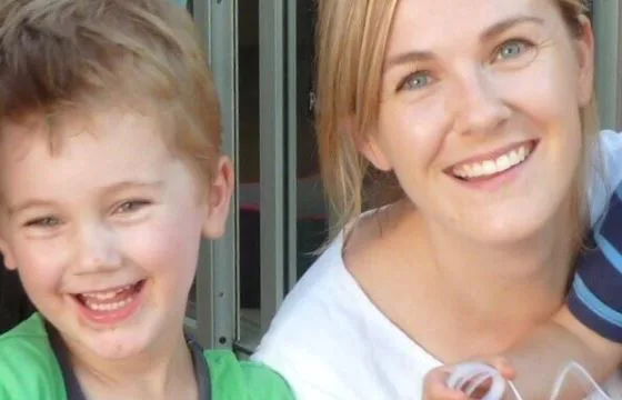 A woman and a child smiling brightly at the camera in an outdoor setting.