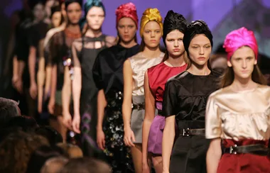Models walking on a fashion runway wearing colorful dresses and headscarves.