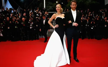 A couple poses on a red carpet with photographers in the background, wearing a black and white gown and a tuxedo.
