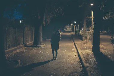 Dark, empty street at night with a lone figure walking away under streetlights.
