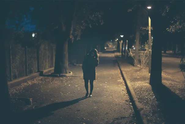 Dark, empty street at night with a lone figure walking away under streetlights.