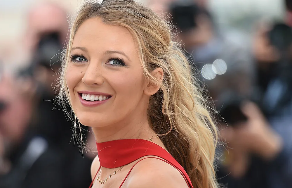 I don't know who this person is, but they're smiling in a red outfit against a blurry background.