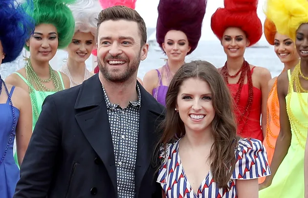 Actors pose with women in colorful dresses and wigs, smiling at a public event.