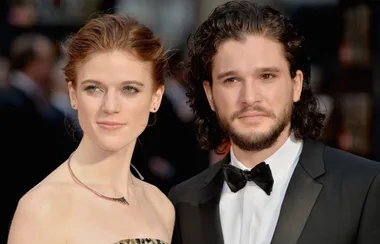 A couple poses elegantly on the red carpet, the woman in a strapless dress and the man in a tuxedo with a bow tie.