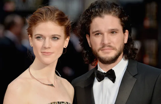 A couple poses elegantly on the red carpet, the woman in a strapless dress and the man in a tuxedo with a bow tie.
