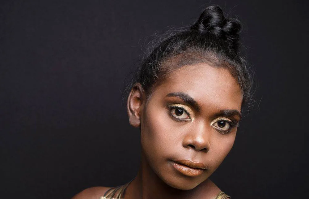 Portrait of a person with elegant makeup and a bun hairstyle against a black background.