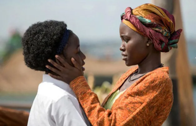 Two women stand close, one holds the other's face gently, against a blurred outdoor background.