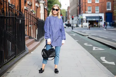 Woman in striped shirt and jeans on a city street, holding a black handbag and wearing sunglasses.
