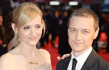 A man and a woman on a red carpet, smiling and dressed formally.