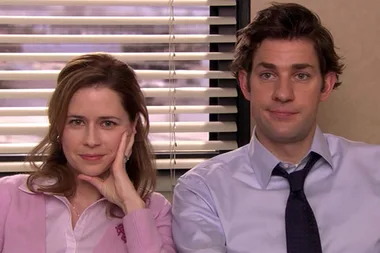 Two people sit close together, with one resting their face on a hand and the other looking at the camera, blinds in background.