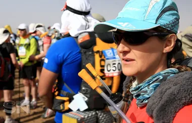 Participants in athletic gear preparing for a desert marathon, one wearing a cap and sunglasses in the foreground.