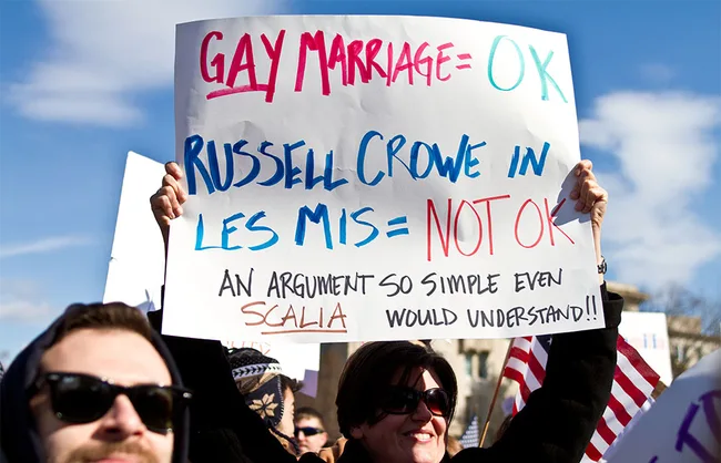 Protest sign reads "Gay Marriage = OK, Russell Crowe in Les Mis = Not OK." People march with signs and flags.