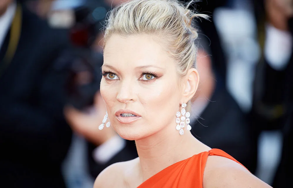 Blonde woman in red dress with dangling earrings at a formal event, staring intently.