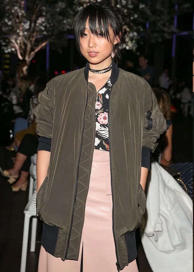 Person wearing a floral top with an army green bomber jacket and pink skirt at an event.
