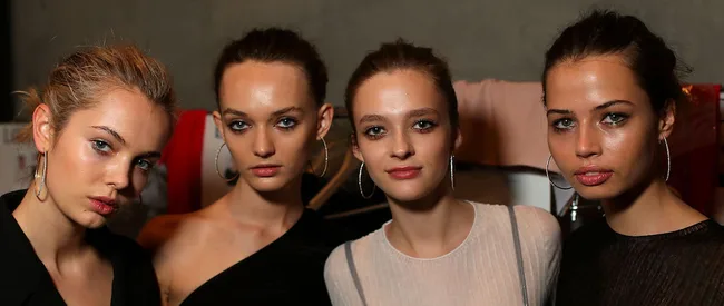 Four women with tied-back hair and hoop earrings posing together.