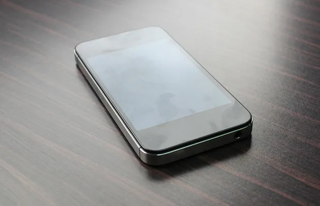 A smartphone with a black screen is placed on a wooden table.