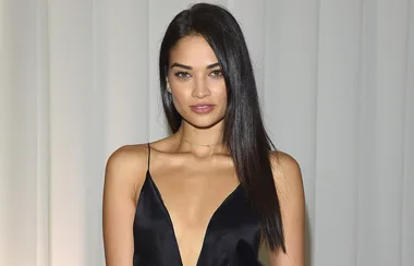 Young woman with long dark hair in a black dress posing against a neutral background.