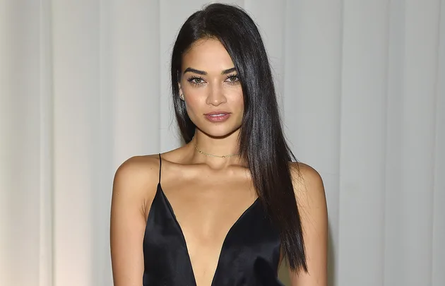 Young woman with long dark hair in a black dress posing against a neutral background.