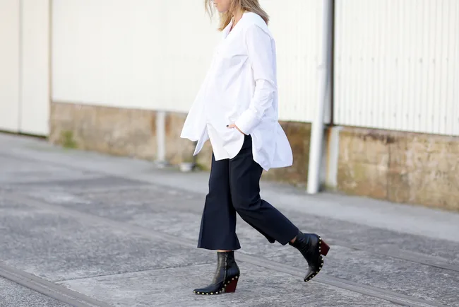 Person in oversized white shirt and black pants walking on a sidewalk.