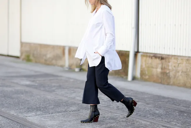 Person in oversized white shirt and black pants walking on a sidewalk.