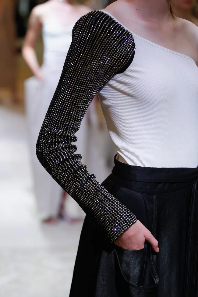 Model wearing a one-shoulder top with black rhinestone sleeve and black skirt.