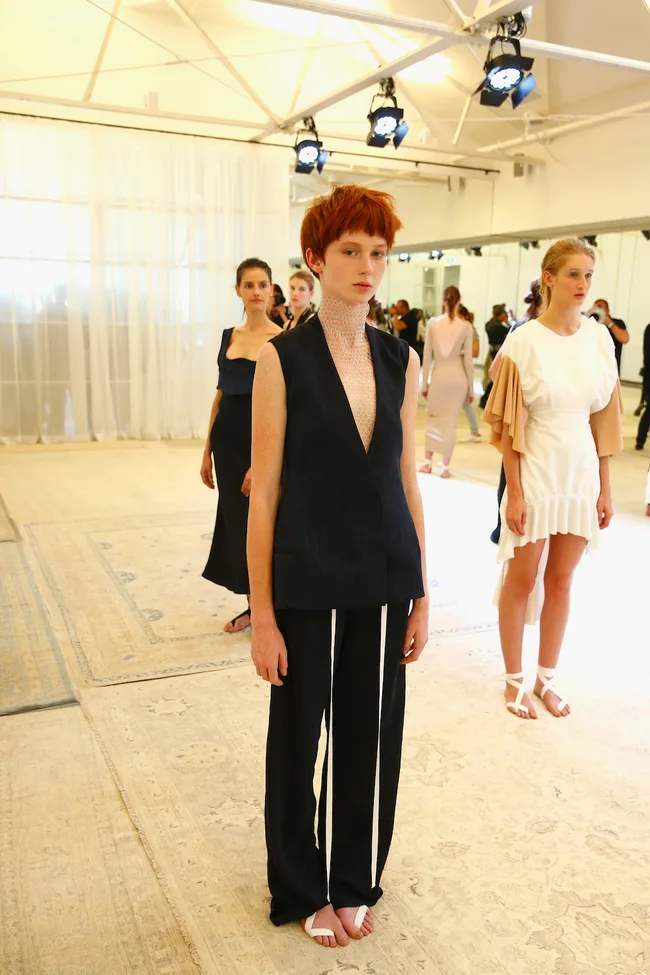 Models standing in a fashion show setting, wearing minimalist contemporary designs with neutral colors.