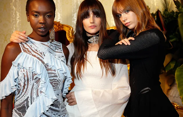Models posing in ornate outfits; one in a blue lace dress, one in white sleeves, and one in black mesh.