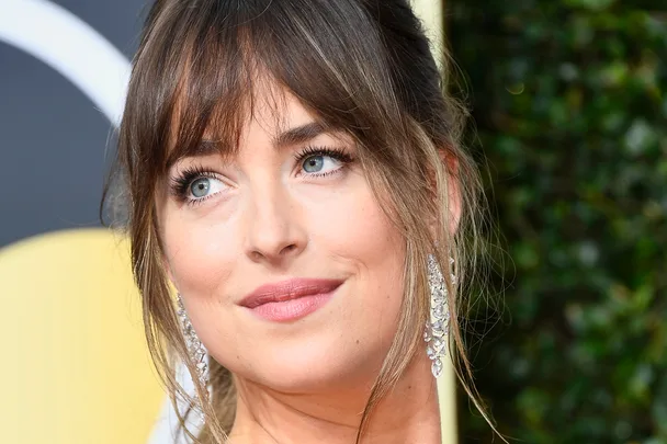 Woman with brown hair and bangs, wearing sparkly earrings, looking to the side at a formal event.