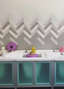 Baby in purple neck float in a baby spa bath surrounded by ducks, with herringbone pattern wall tiles.