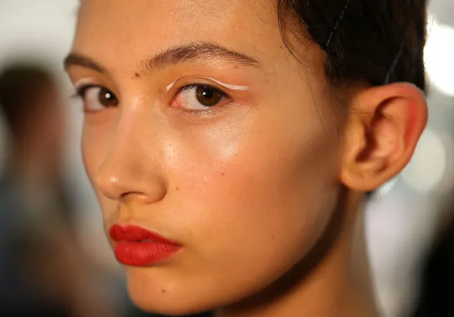A model with bold red lipstick and subtle makeup gives a side glance, showcasing a fresh and radiant look.