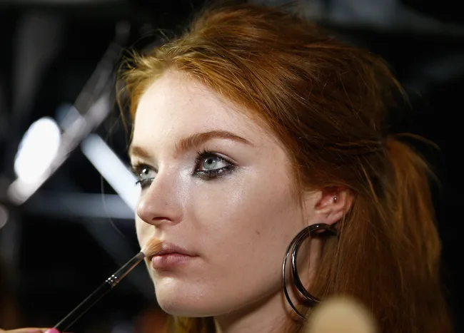 Model with red hair gets makeup applied backstage.