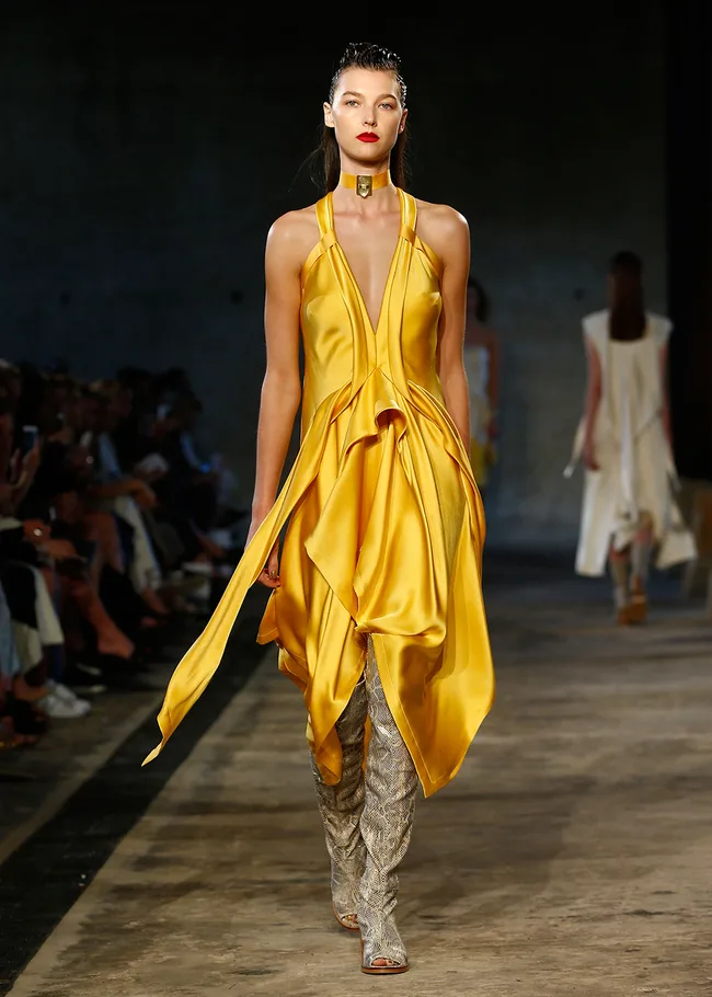Model in a flowing yellow dress walks the runway during a fashion show.