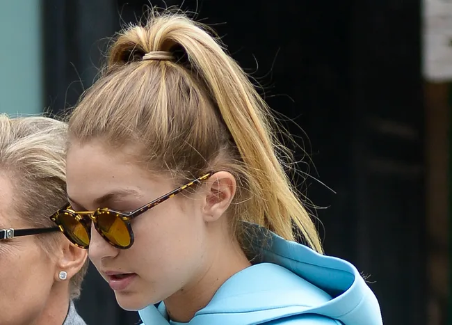 A person in sunglasses outside wearing a blue hoodie with hair in a ponytail.