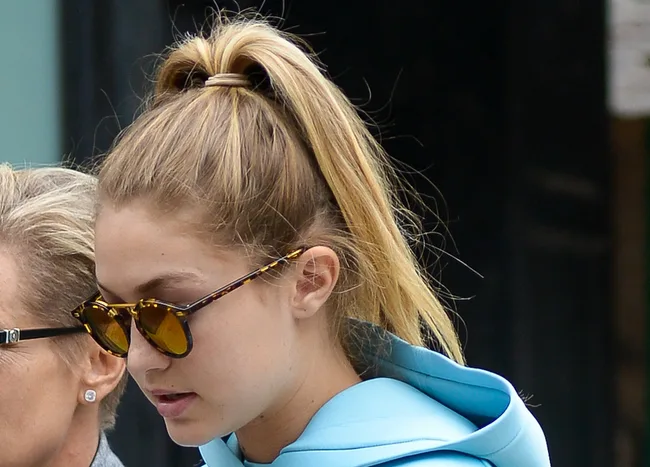 A person in sunglasses outside wearing a blue hoodie with hair in a ponytail.