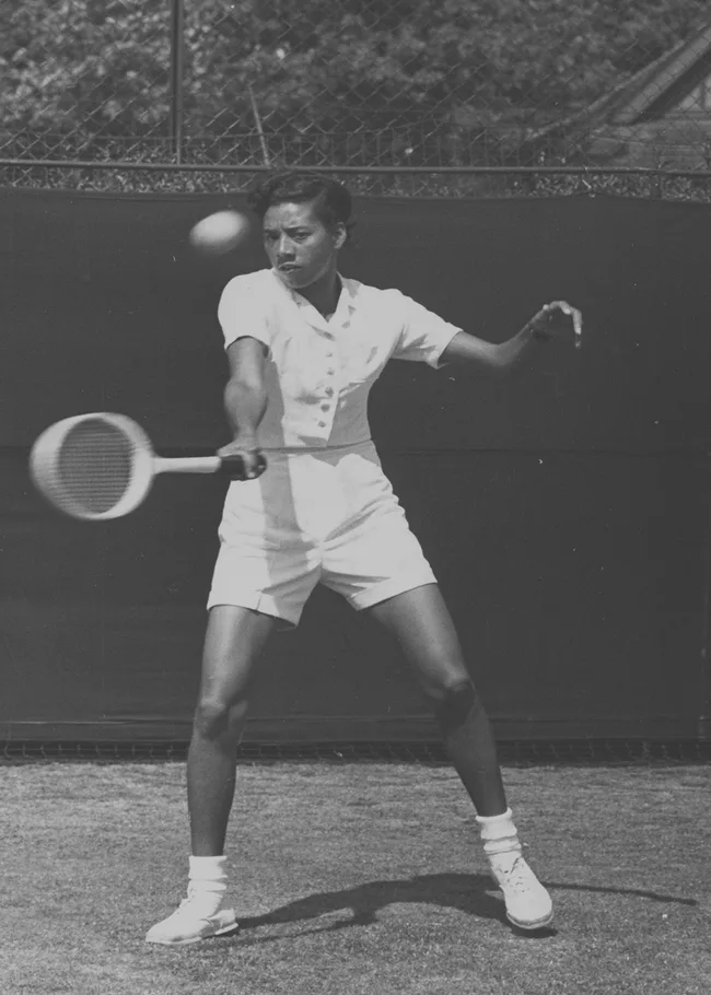 A tennis player in a white outfit hits a forehand shot on a grass court.