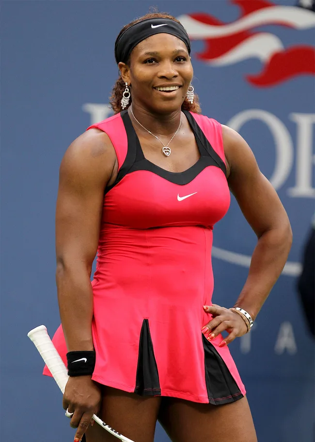 Tennis player in a red and black outfit holding a racket, smiling on a tennis court.